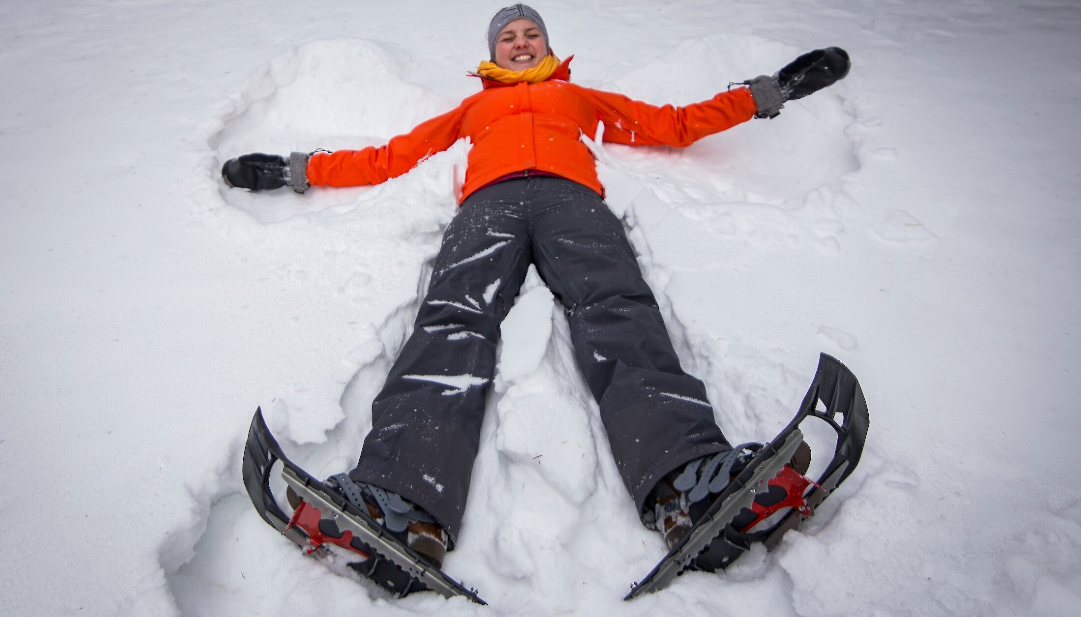 A woman making a snow angel in the snow whilst wearing snowshoes