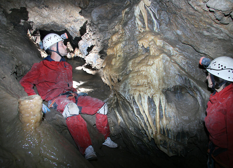 Two people in rat nest cave looking at rock formations on a cave tour