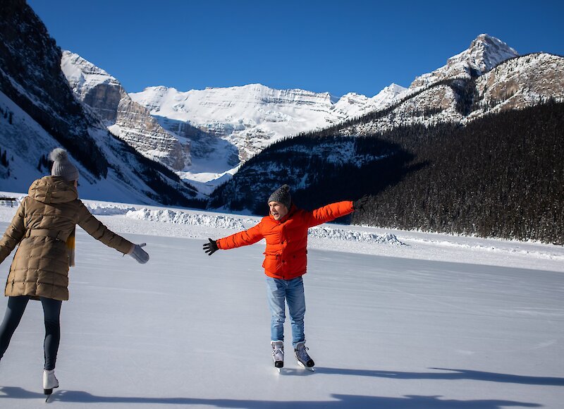Couple ice skating on Lake Louise in winter looking happy