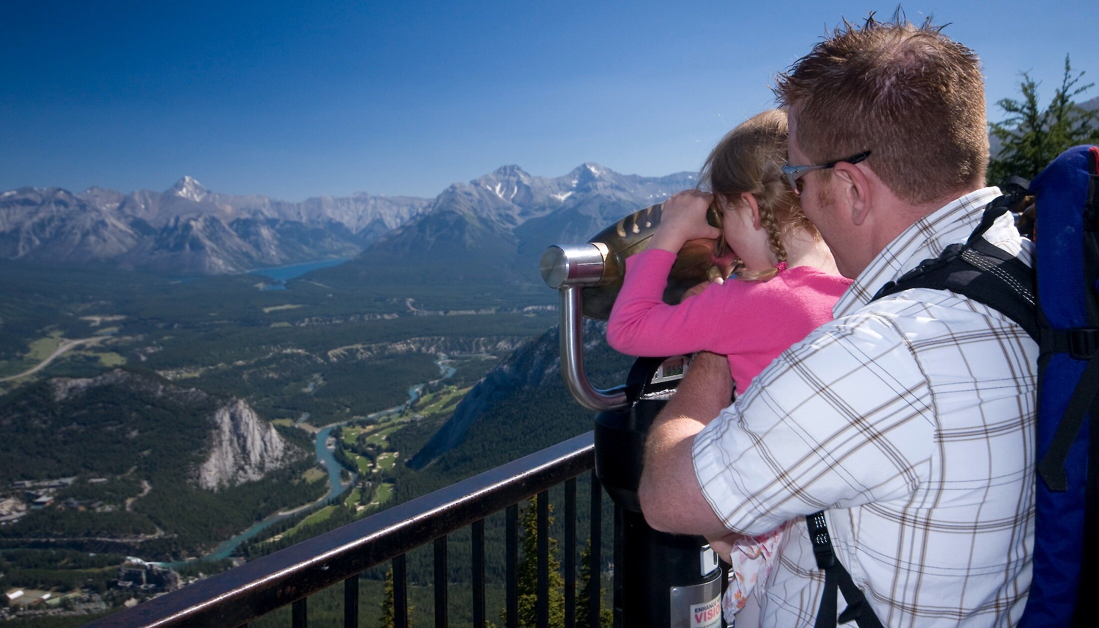 A little girl being held by her dad looking through a tower viewer on the Banff Gondola viewing deck