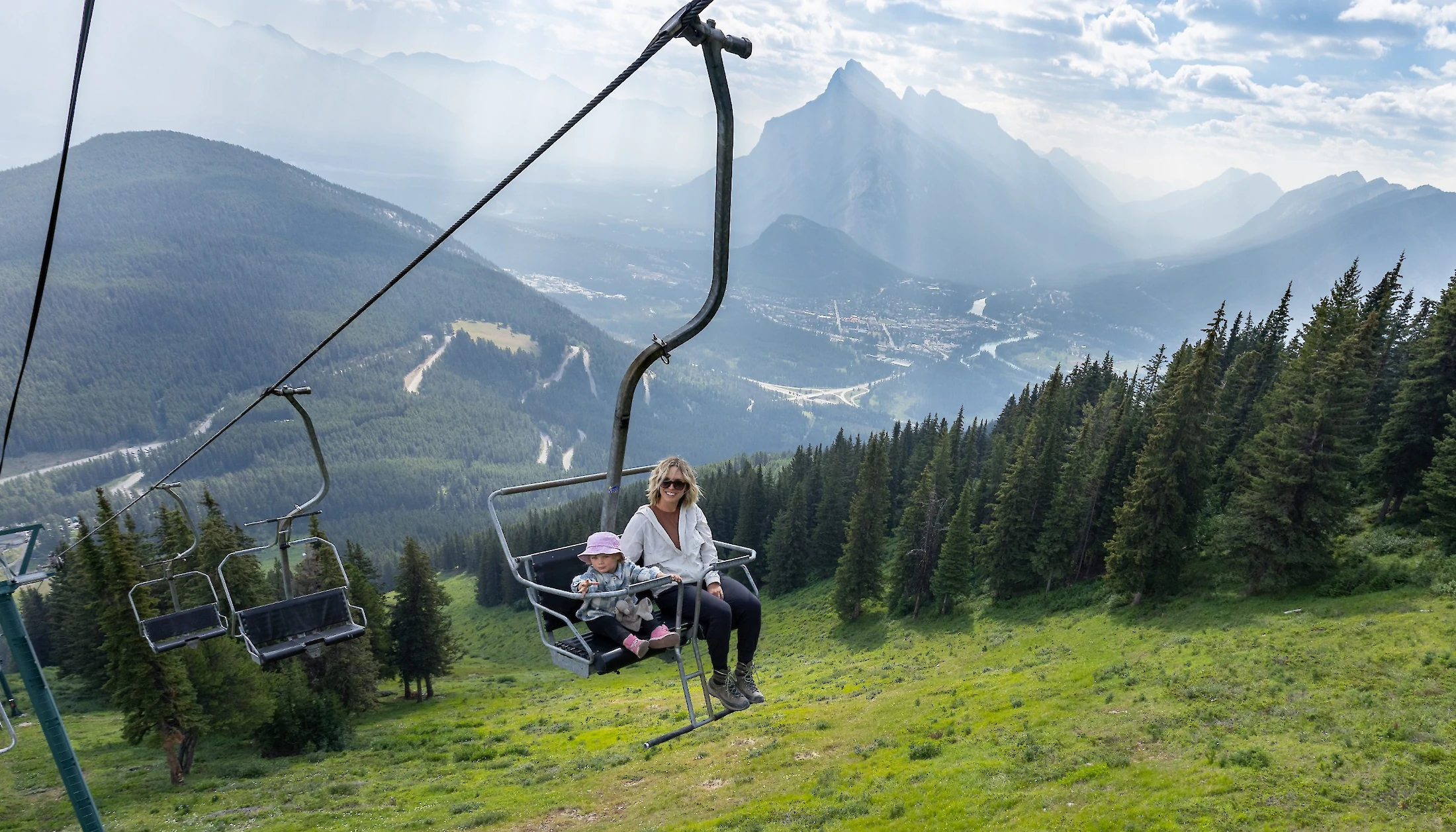 Mother and child riding up the Mount Norquay Chairlift with a mountain view background