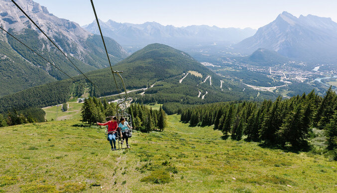 Two people riding up the Mount Norquay Chairlift with a mountain view background