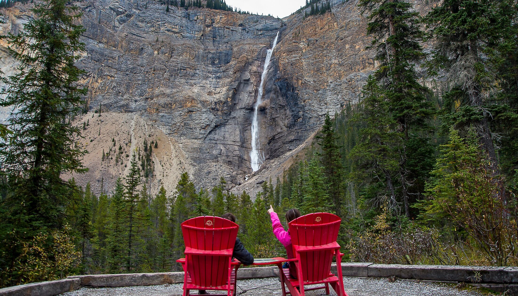 Two people sitting on red chairs looking at Takakkaw Falls