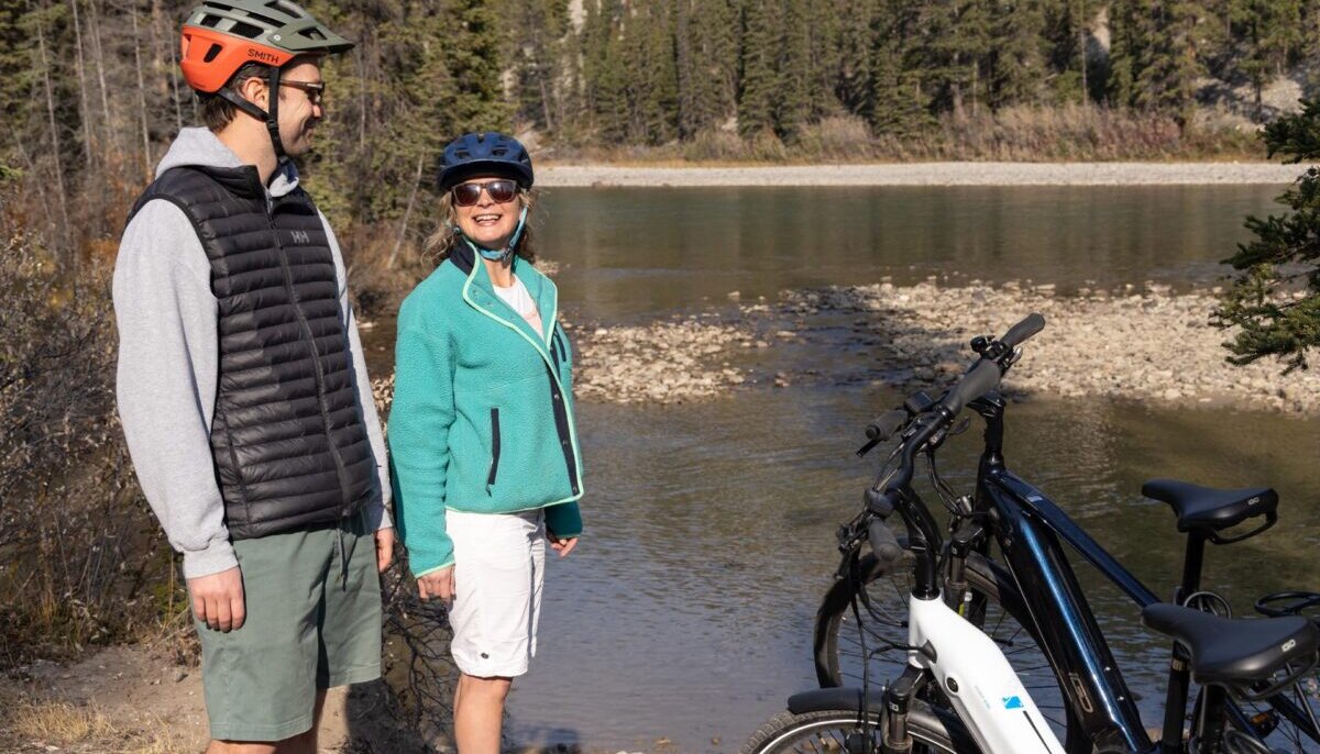 A couple in front of the Bow River with their E bikes in Banff