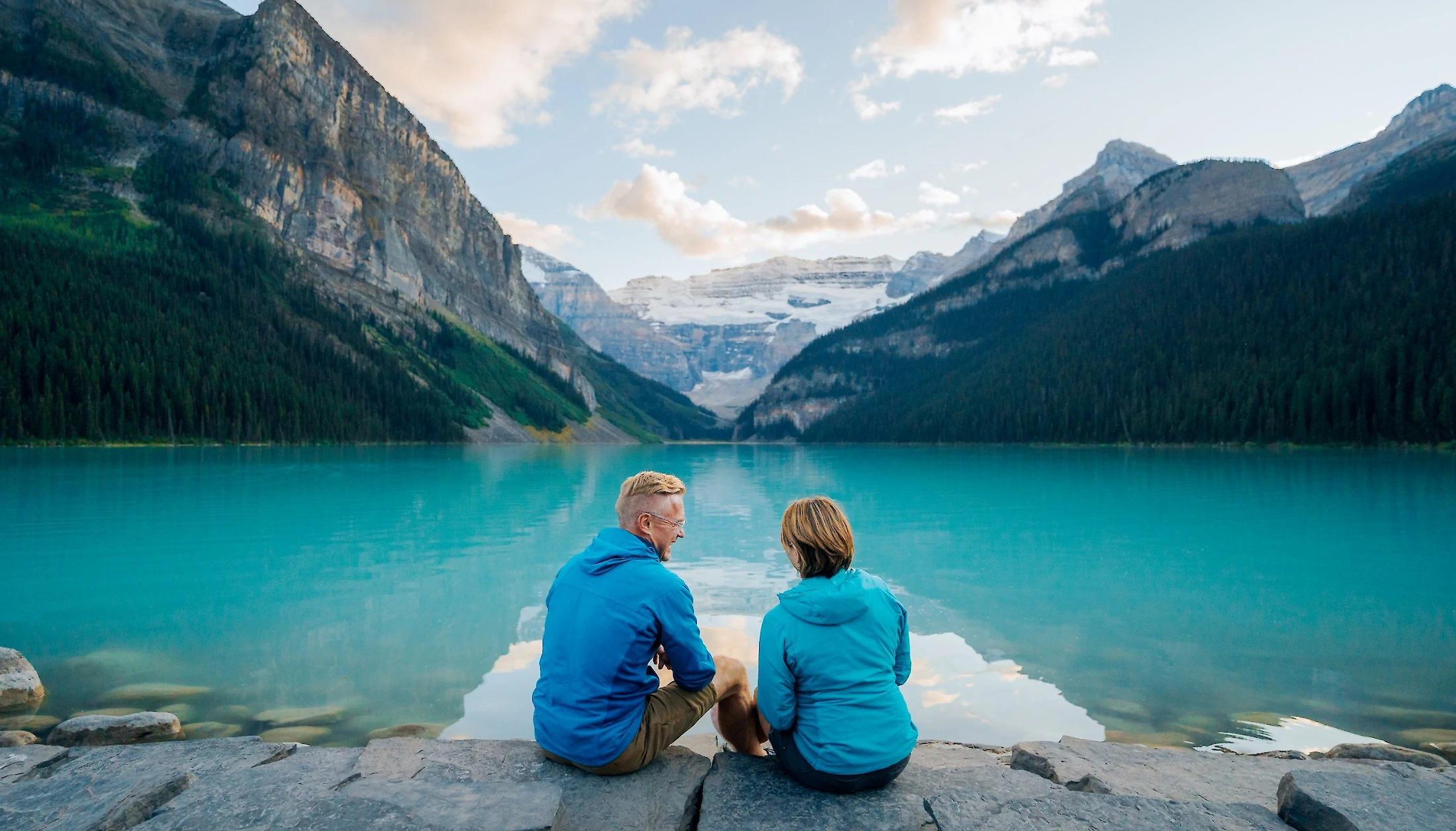 A couple overlooking the sunset at Lake Louise from the shore.