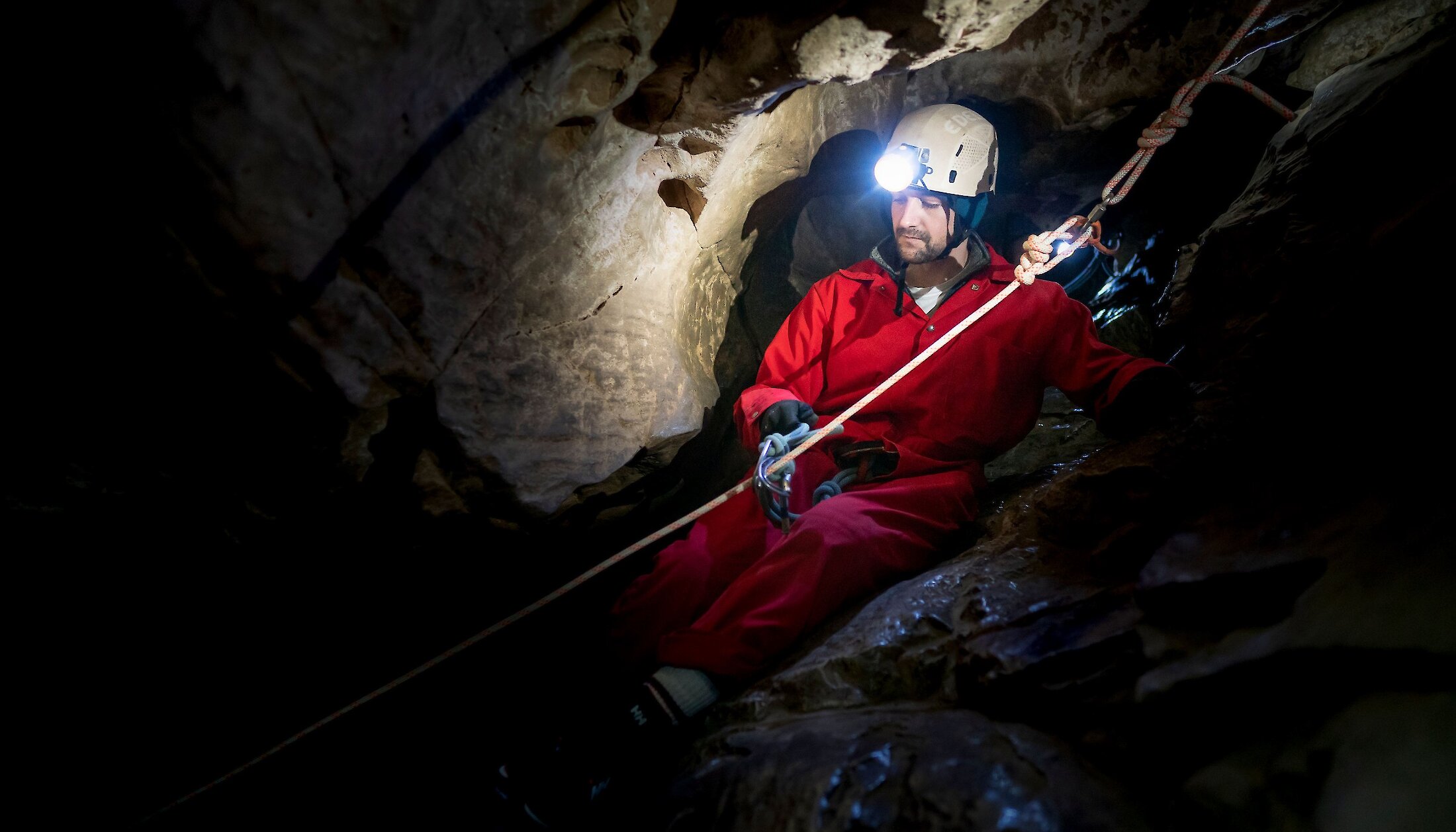 A man sliding down some rocks using a rope on a cave tour in Canmore