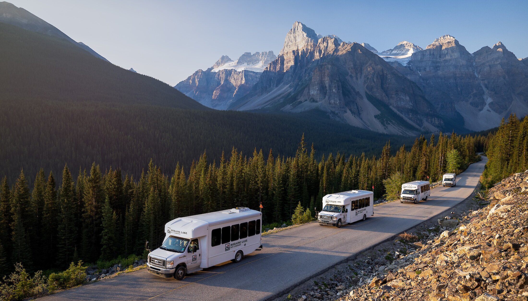 A convoy of Moraine Lake shuttle bus driving the lake road with picturesque mountain views