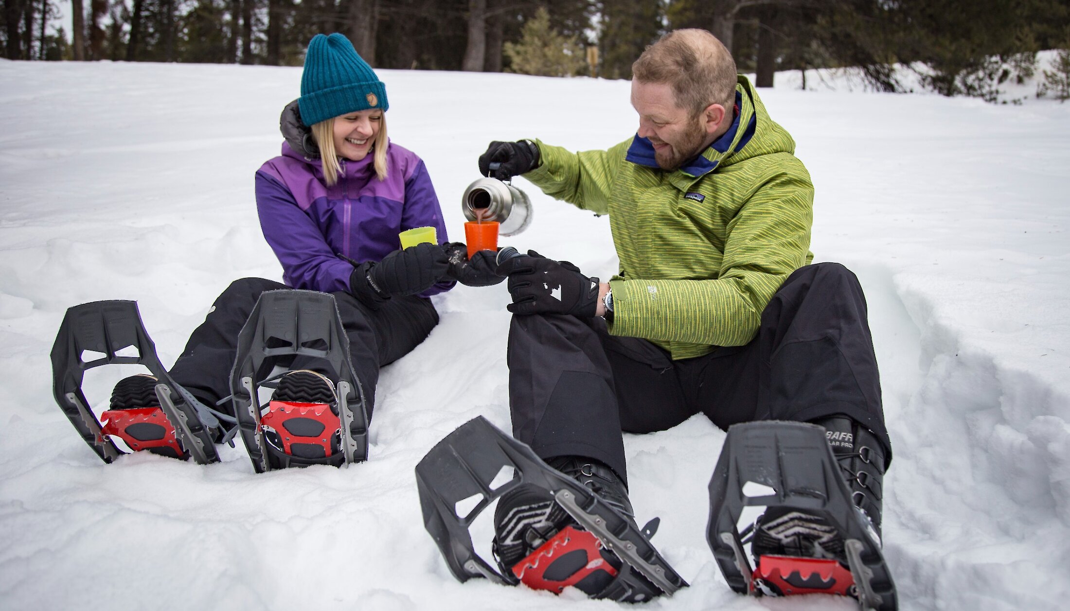 Two people sharing hot chocolate in the snow on the snowshoe tour