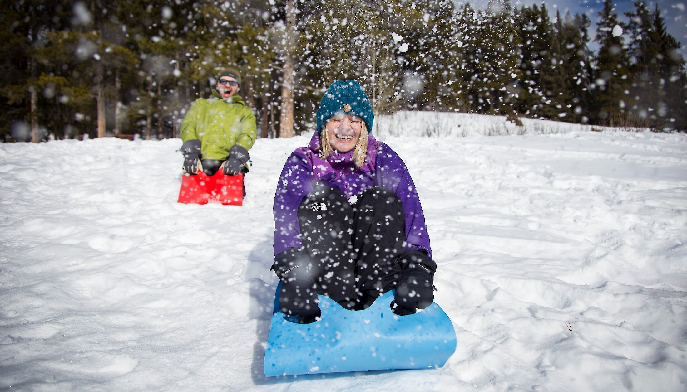 Two people sliding down a small slope on a carpet on a snowshoe tour