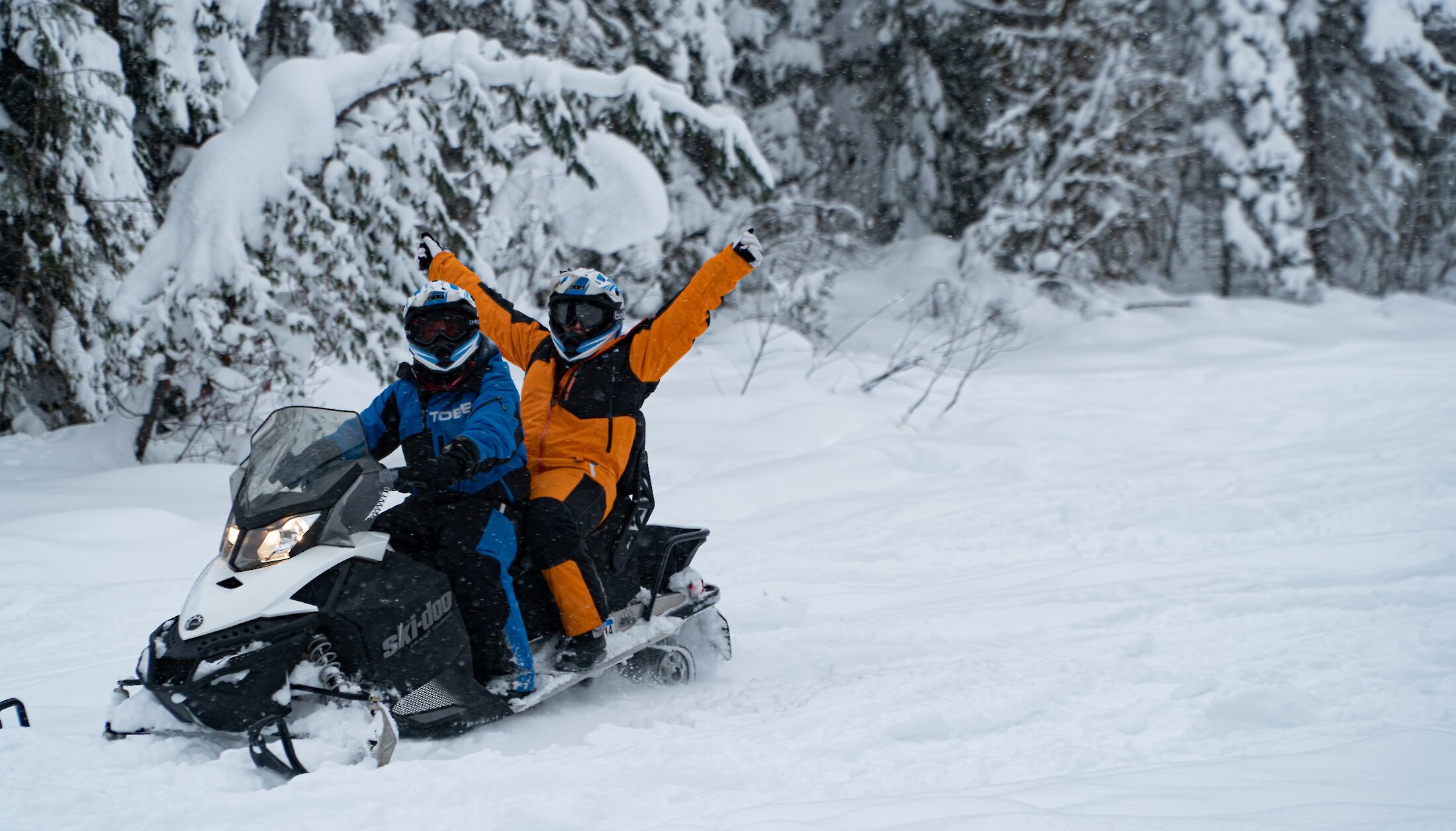 Two people enjoying fresh snow on snowmobile trails in Kicking Horse