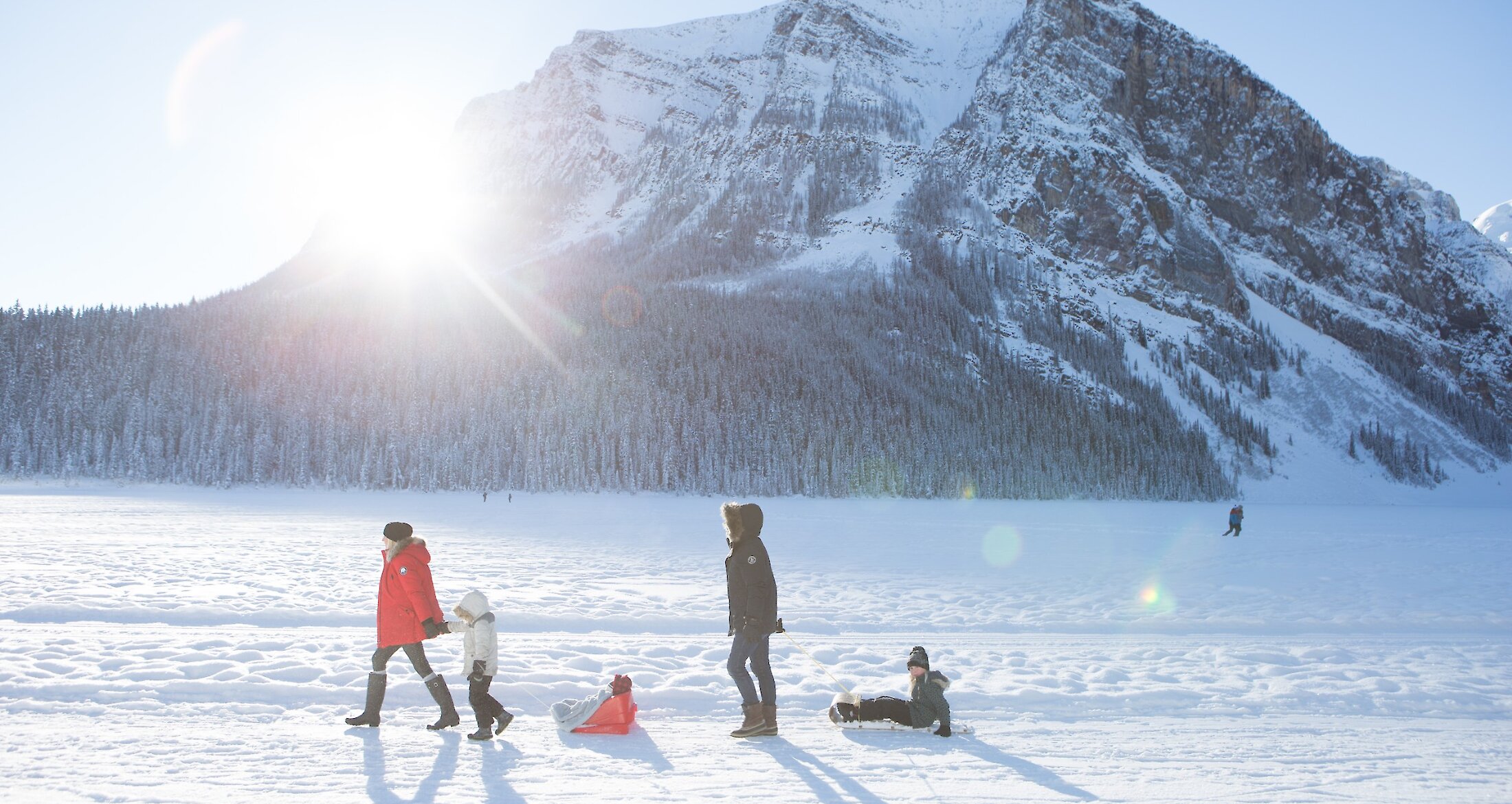 A family walking along Lake Louise Lake Shore with children in sleds