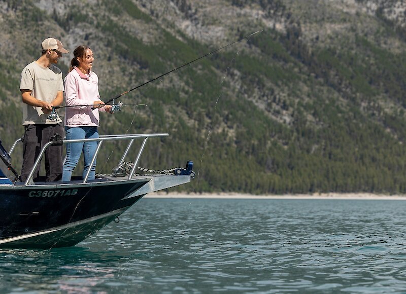 A couple fishing on Lake Minnewanka on the bow of the boat