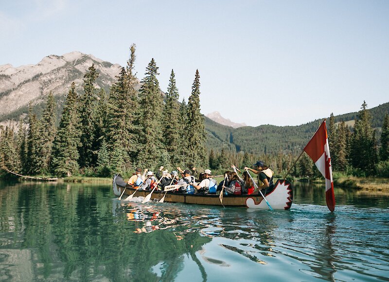 A big canoe tour paddles on the bow river towards Cascade Mountain