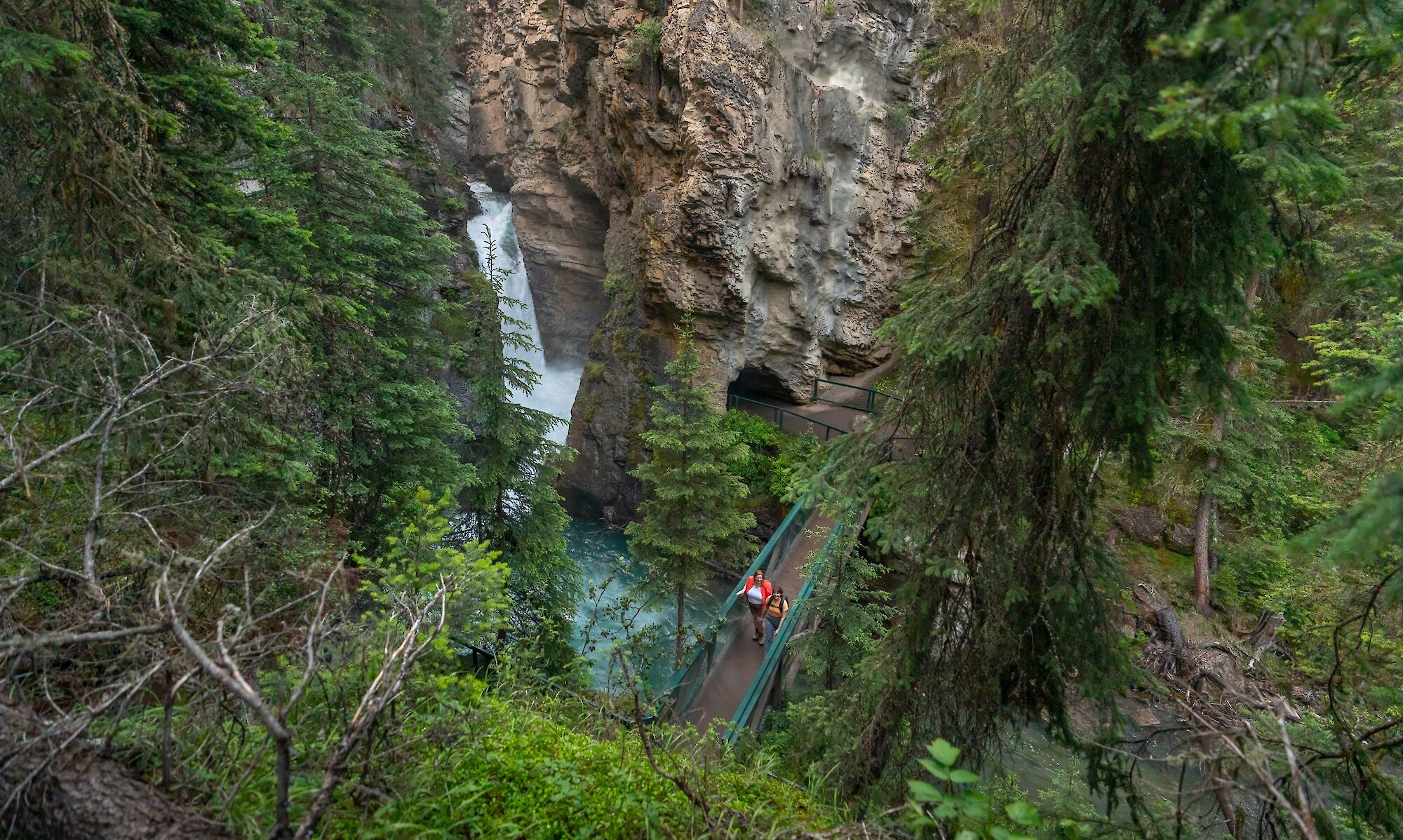 A couple walking across the bridge at the lower falls of Johnston Canyon