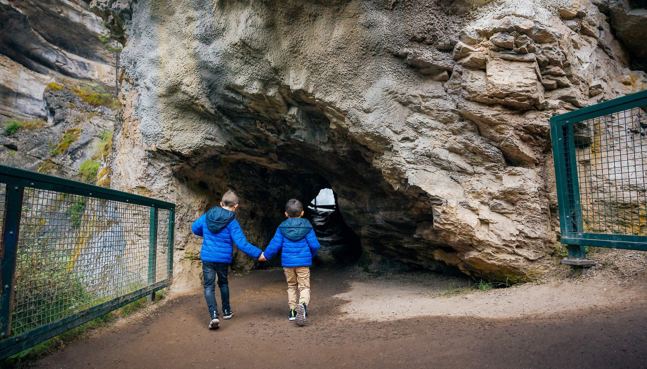 Two children walking through the cave at the Lower Falls at Johnston Canyon
