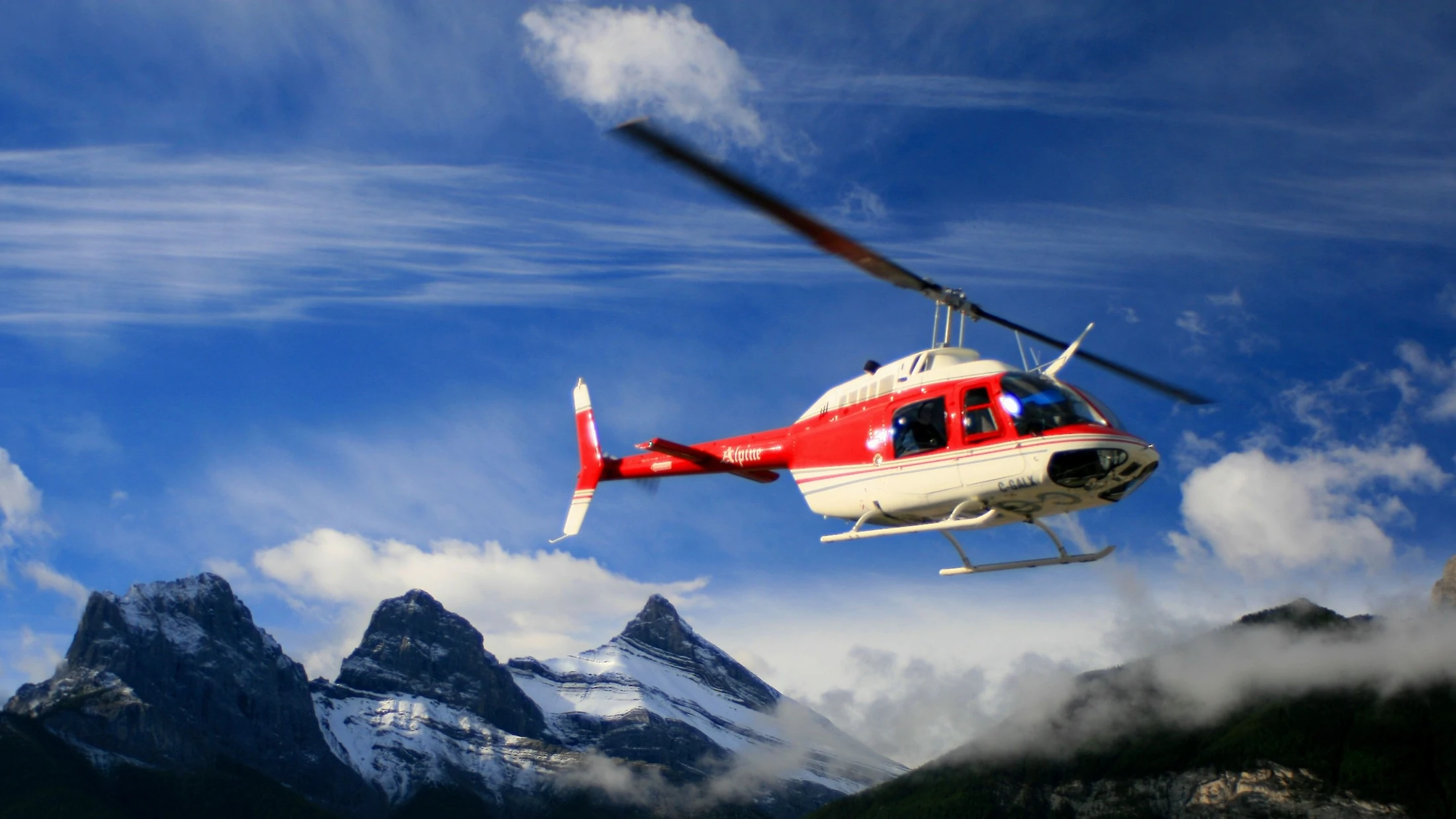 A helicopter flying with Three Sisters Mountains in the background
