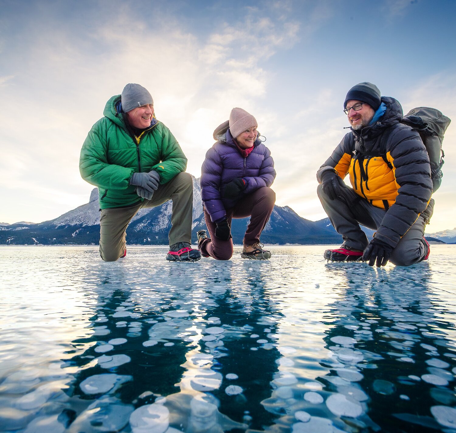 A couple with their guide standing on frozen Abraham Lake looking at the ice bubbles.