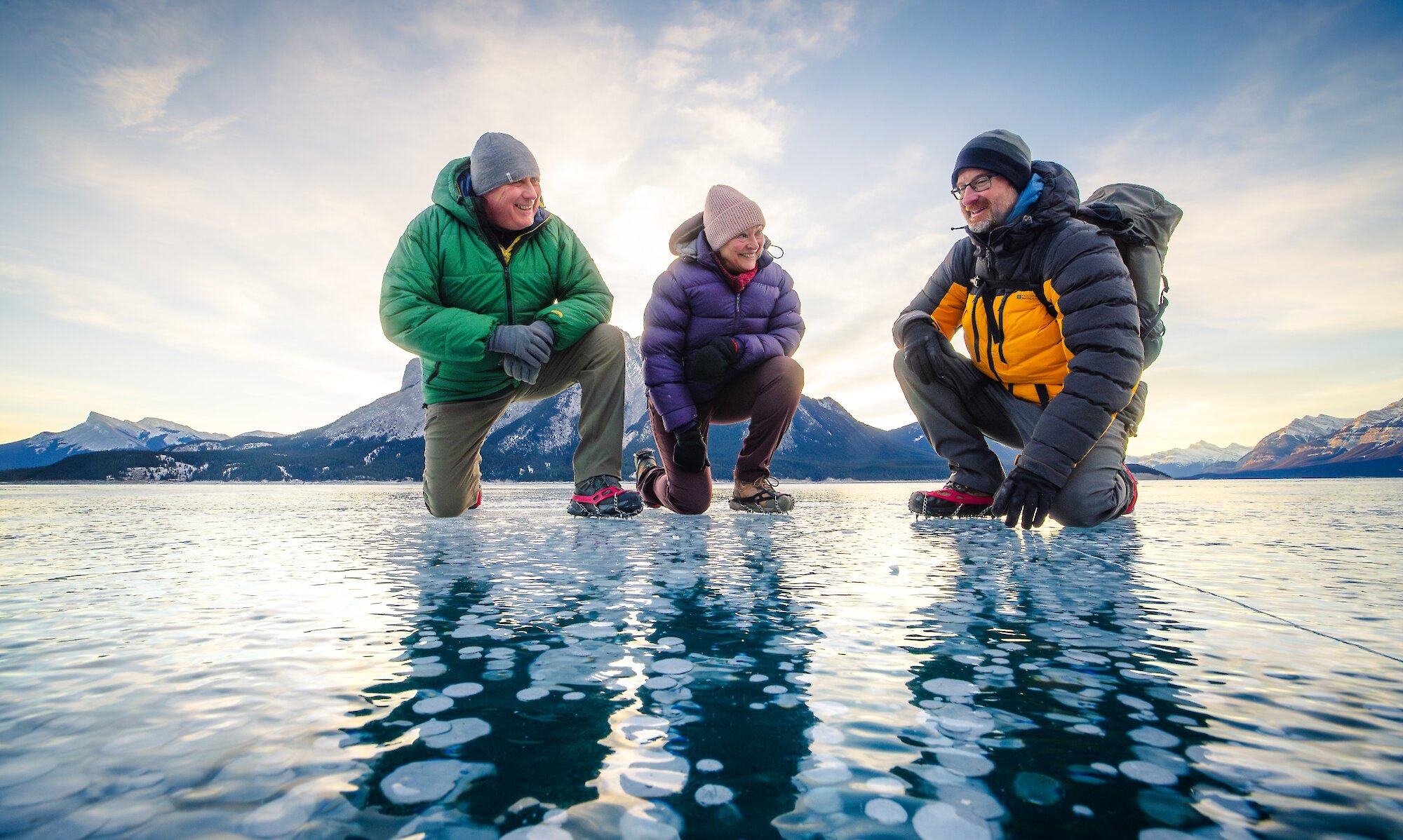 A couple with their guide standing on frozen Abraham Lake looking at the ice bubbles.
