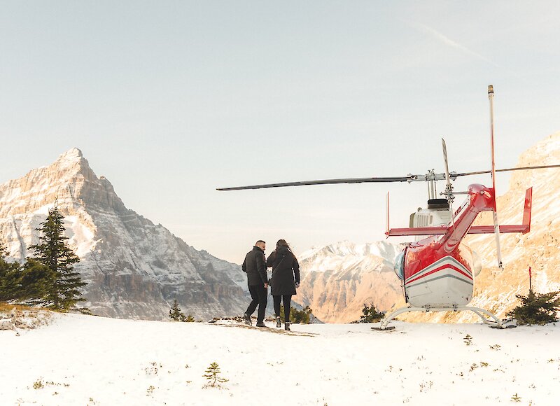 A couple walking towards the helicopter on a mountain landing point.