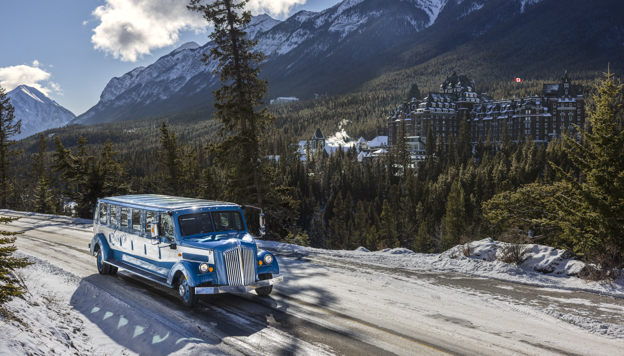 The vintage 1930s open top bus driving with the Fairmont Banff Springs in the background