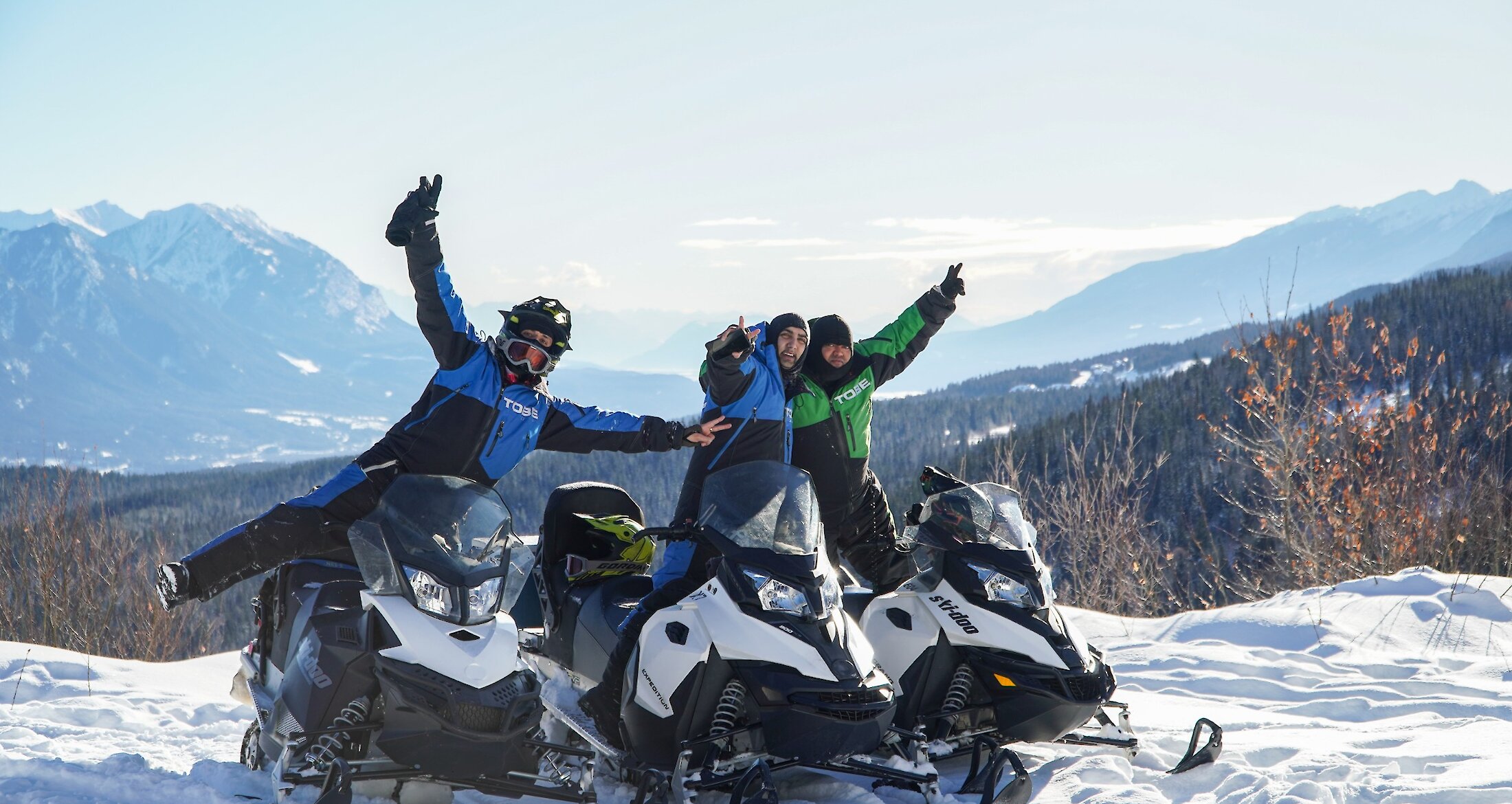 A group of friends enjoying snowmobiling in Kicking Horse with a view of the mountains