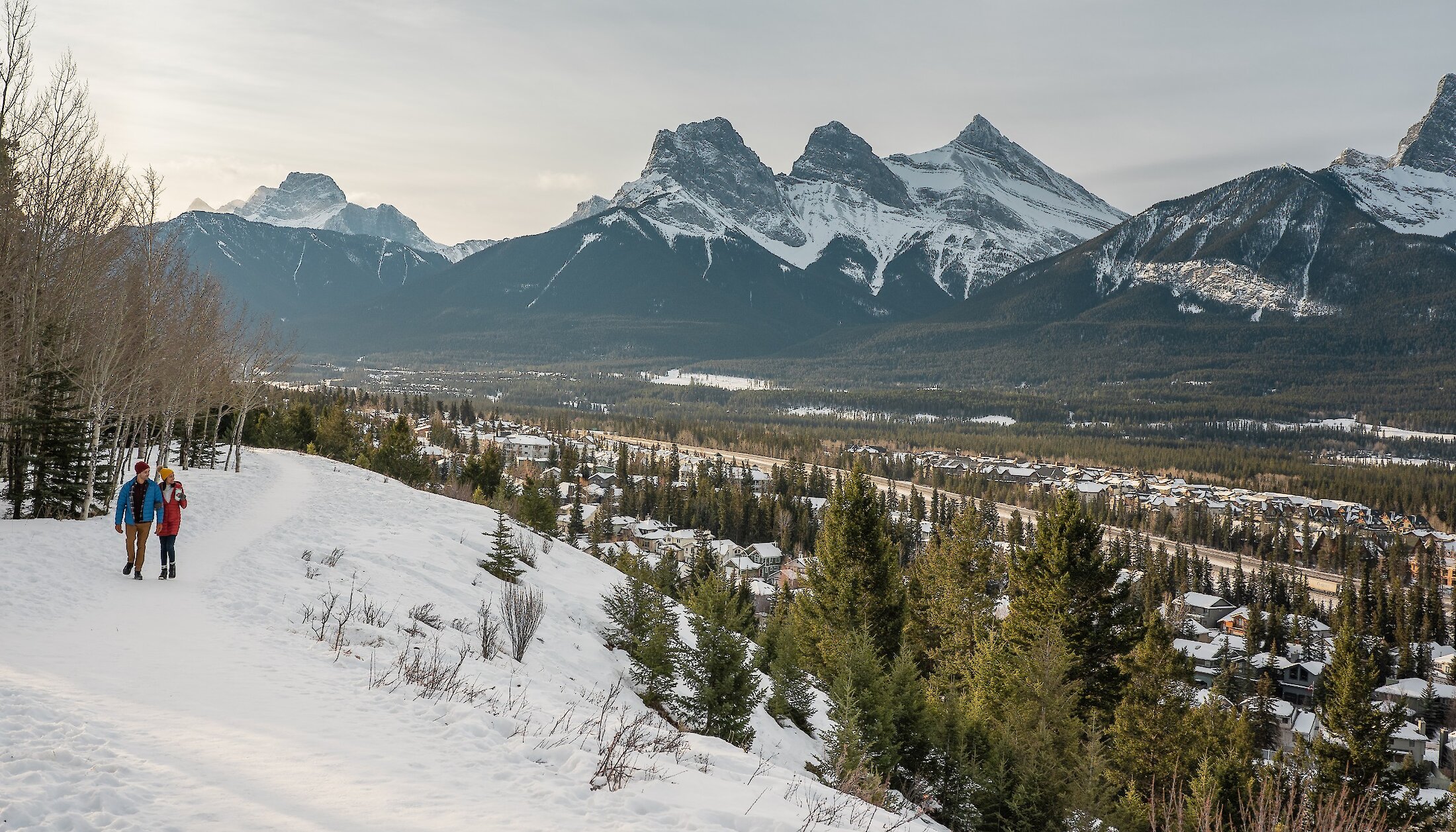 A view of Canmore Town from a snowy trail with a couple walking