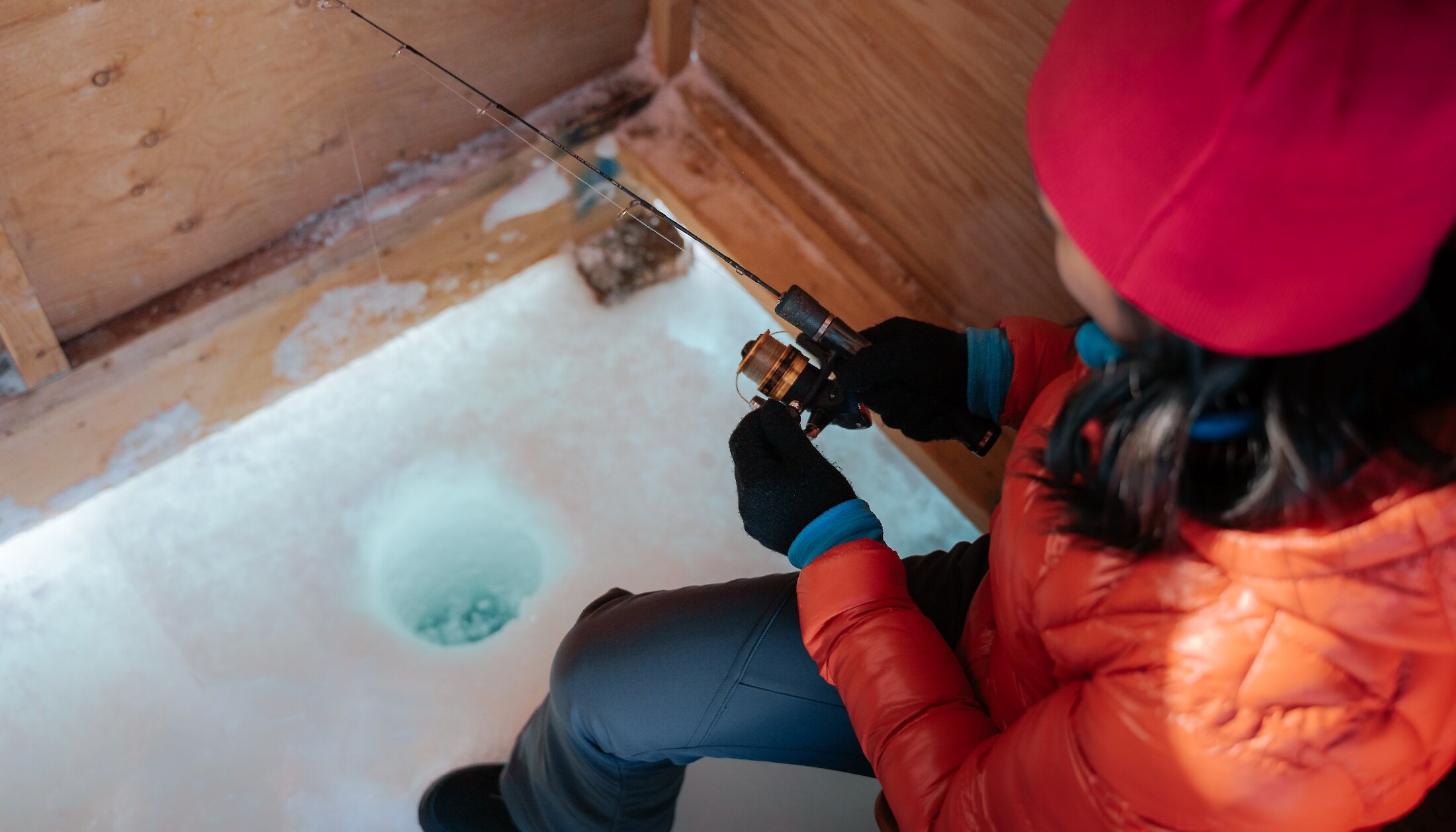 A woman ice fishing in Canmore from inside the hut