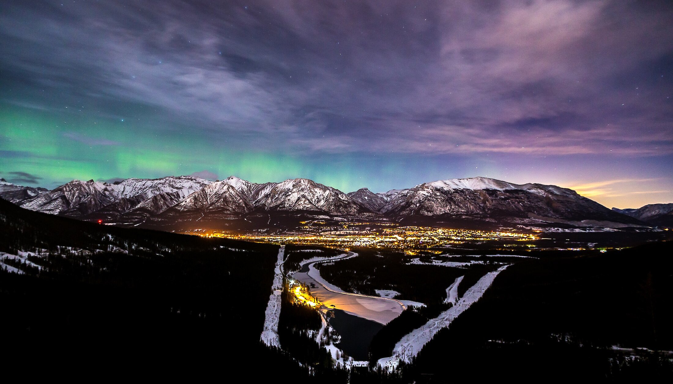 A view of Canmore at night with the aurora borealis in the sky