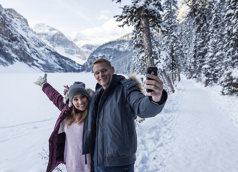 A couple taking a photo in front of a snowy Lake at Lake Louise