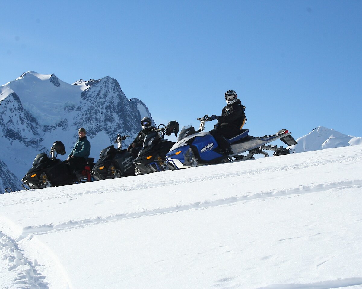 People driving snowmobiles on a bluebird day at Kicking Horse Mountain