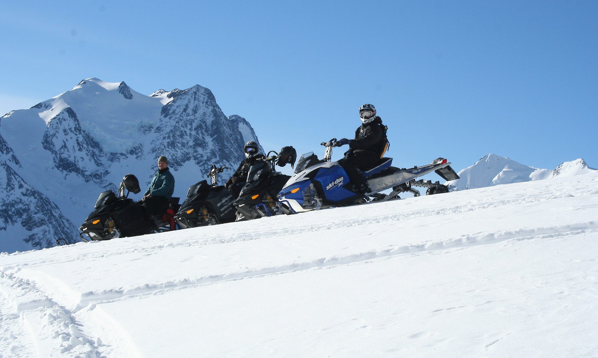 People driving snowmobiles on a bluebird day at Kicking Horse Mountain