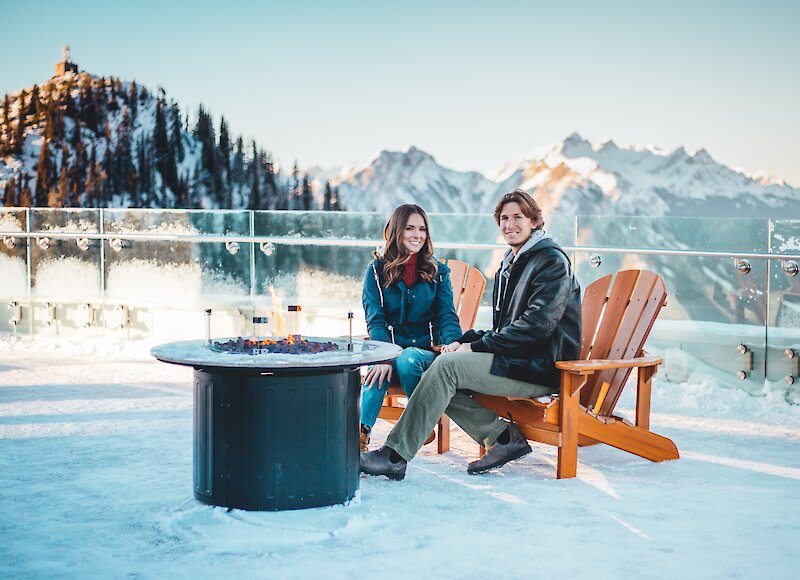 A couple sitting by the fire on the Banff Gondola viewing deck