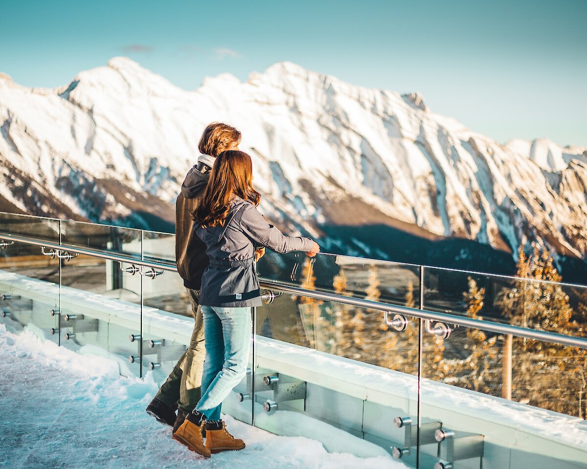 A couple looking out at the Rocky Mountains on the Banff Gondola viewing deck in winter