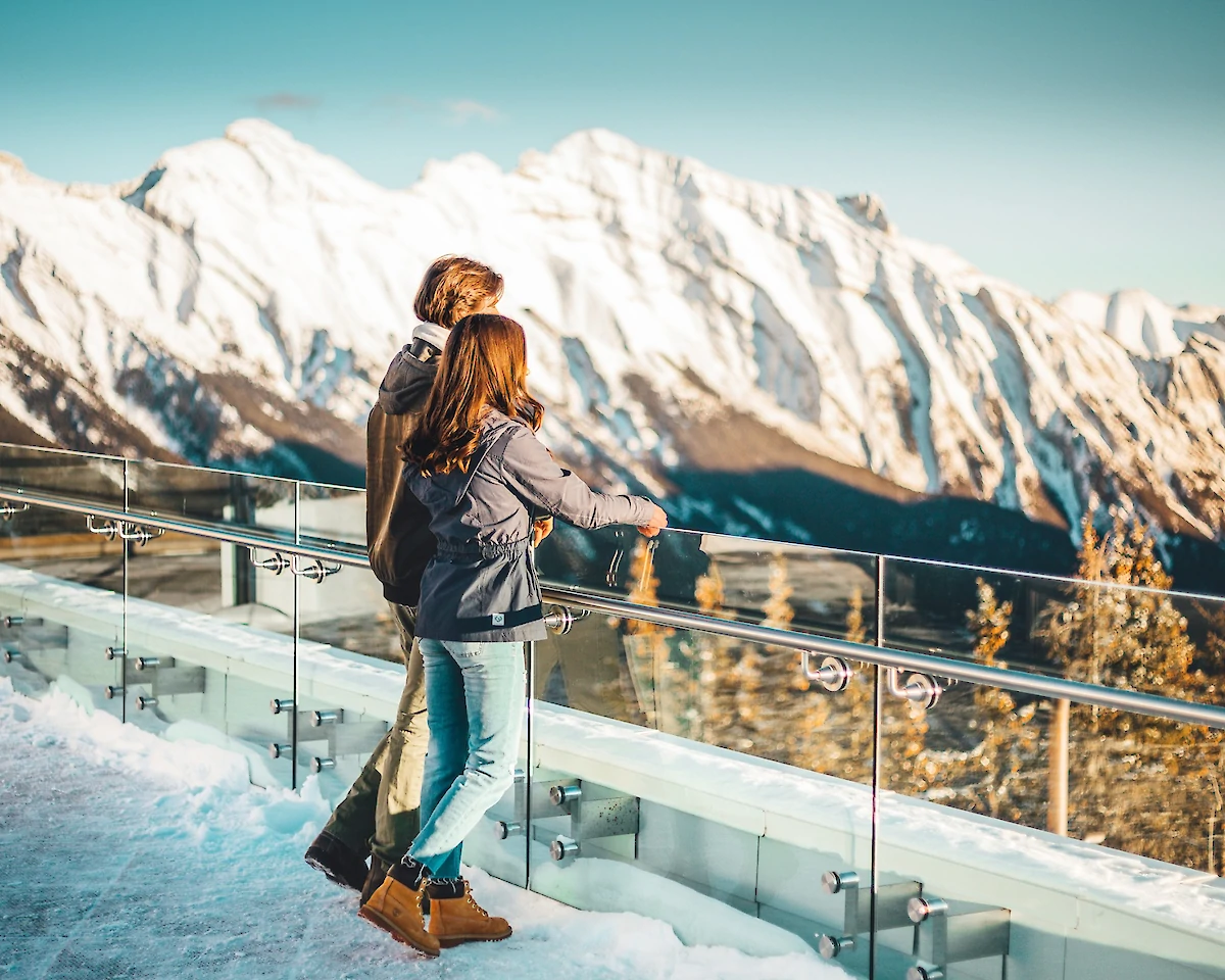 A couple looking out at the Rocky Mountains on the Banff Gondola viewing deck in winter