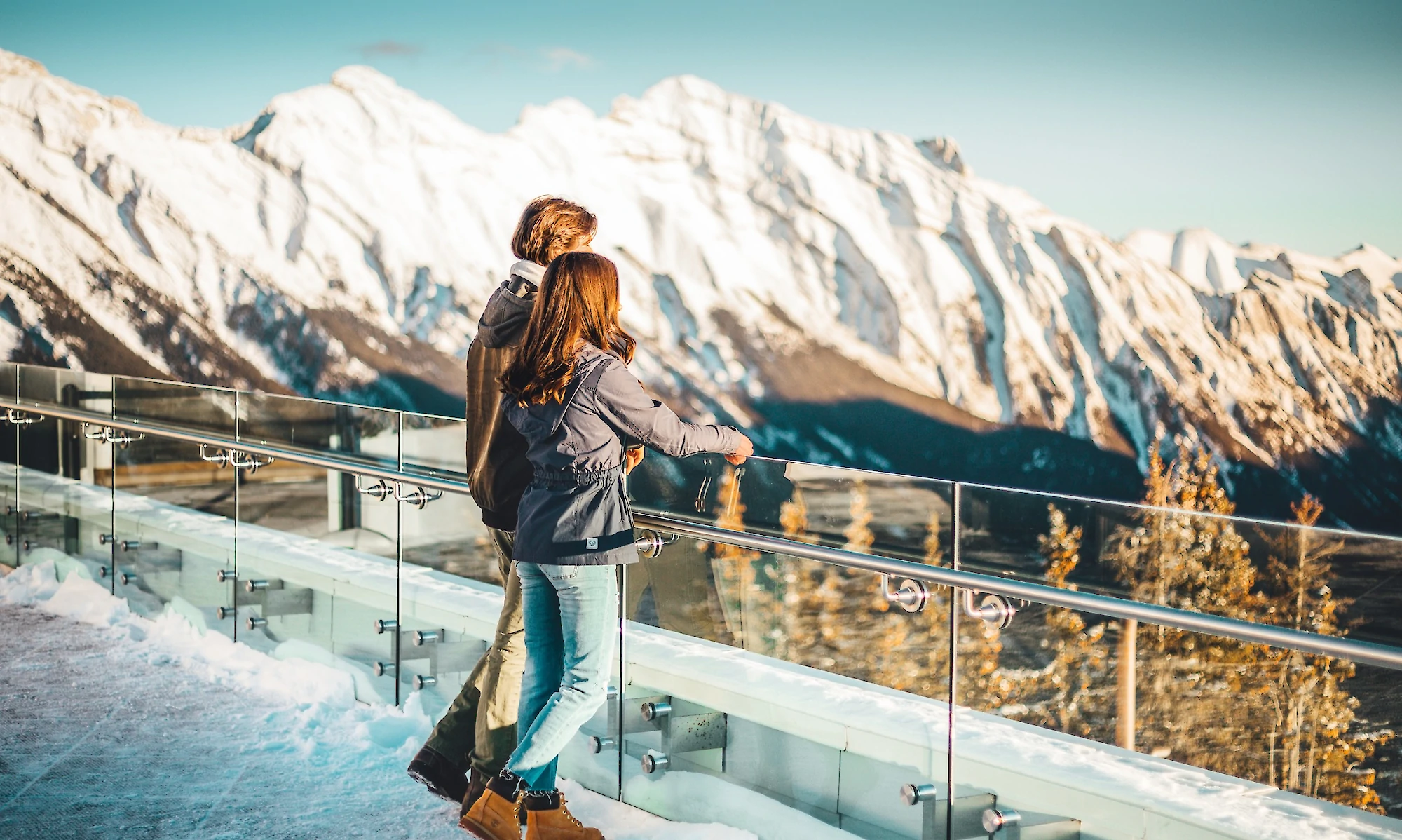 A couple looking out at the Rocky Mountains on the Banff Gondola viewing deck in winter