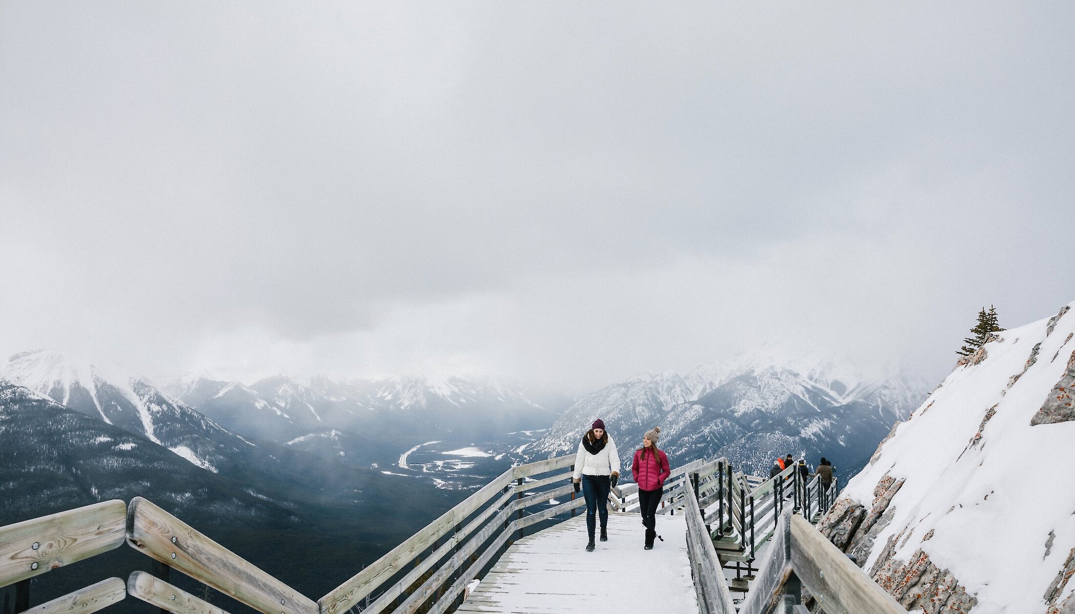 Two people walking along the snowy boardwalk of the Banff Gondola in winter