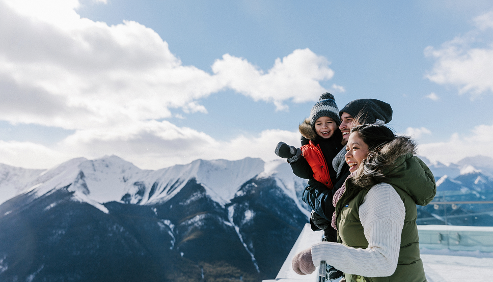 A family on the Banff Gondola viewing deck looking out at the mountains in winter