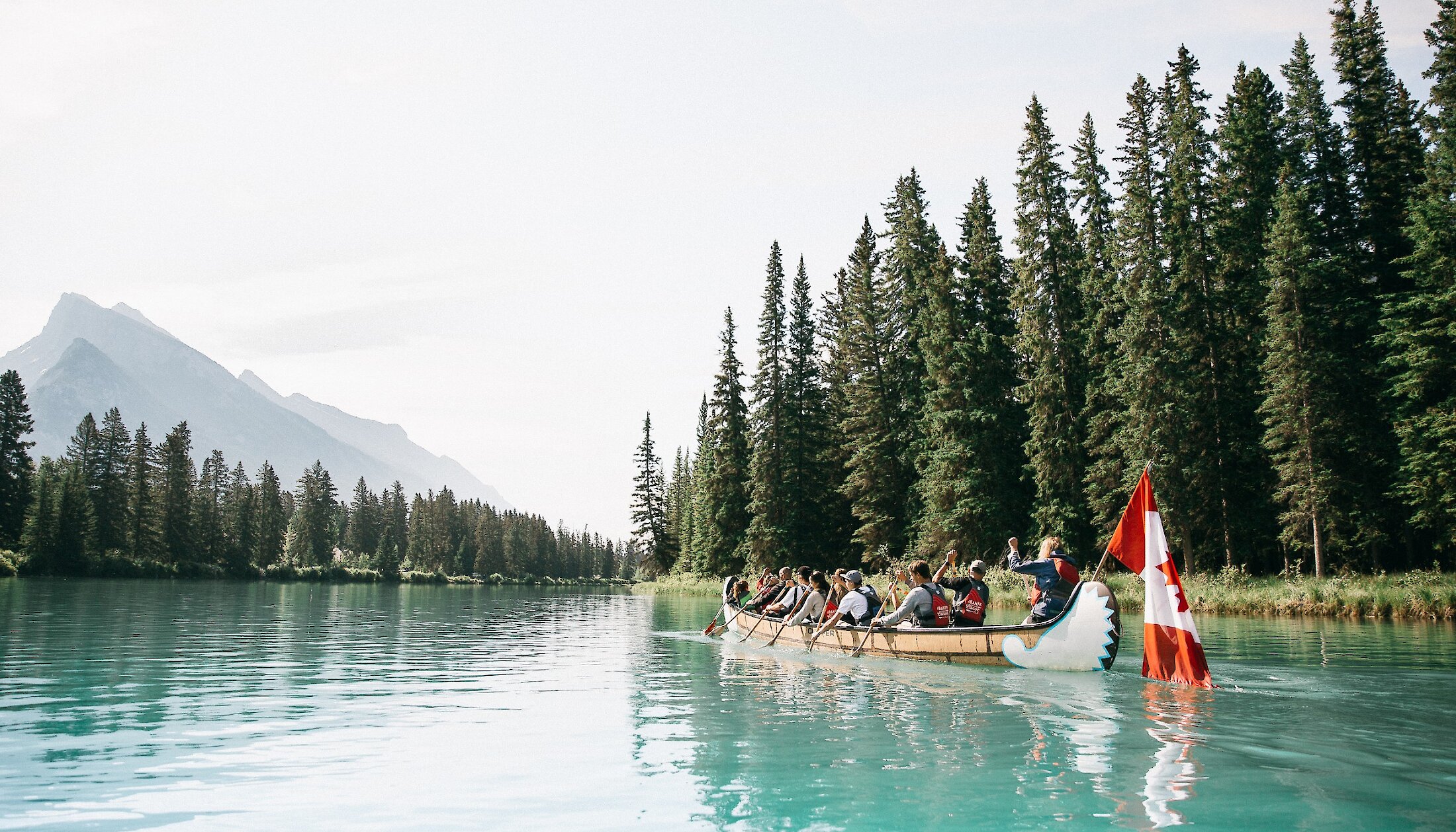 A Big Canoe tour heading down the Bow River with mountain views in Banff