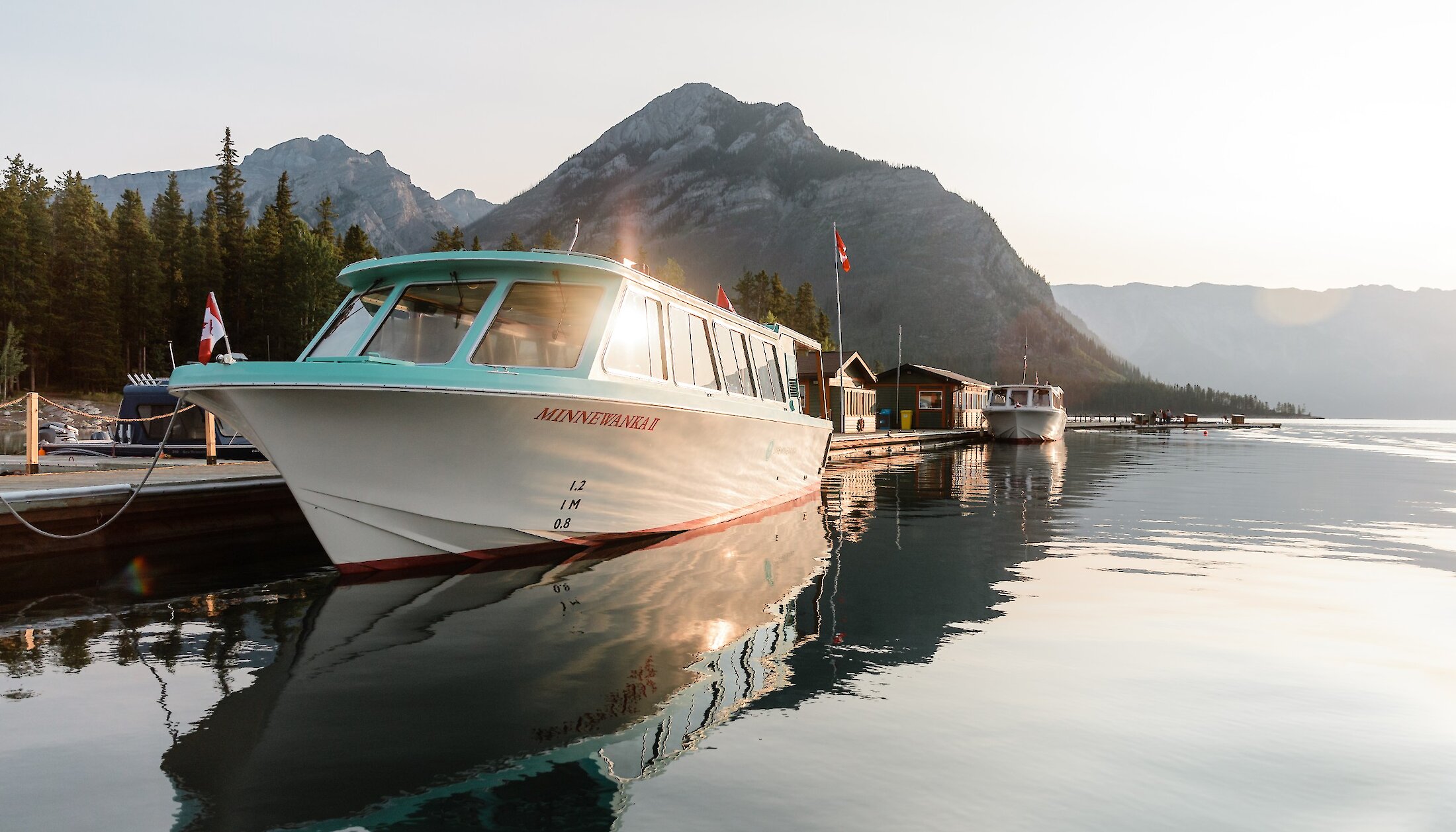 A boat on lake minnewanka during sunset with the mountains surrounding