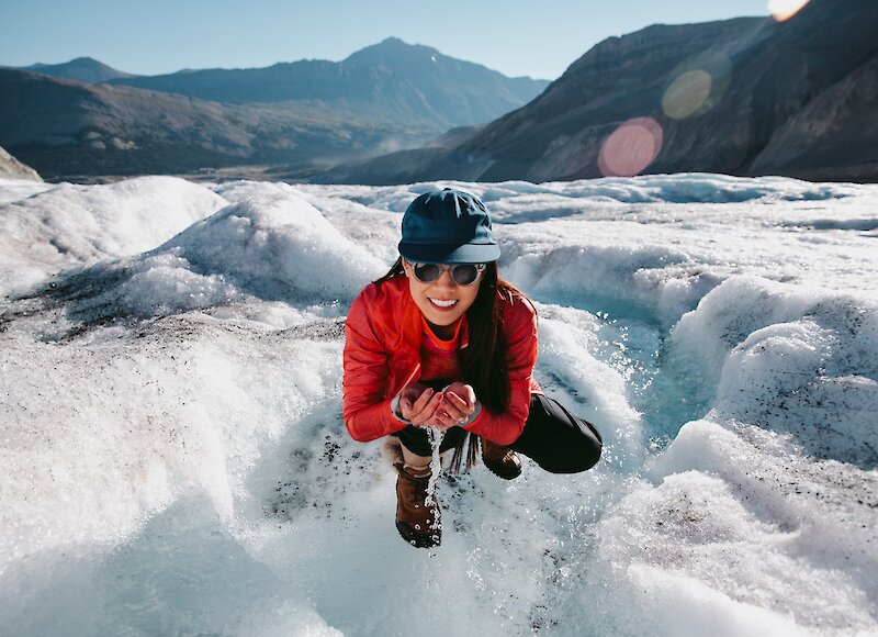 A lady scooping up fresh glacier water at the Columbia Icefields