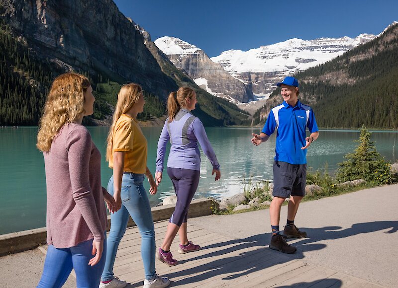 A tour guide talking to guests while walking the Lake Louise shoreline.