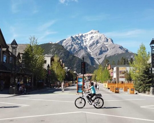 People cycling Ebikes on Banff Ave in front of Cascade Mountain