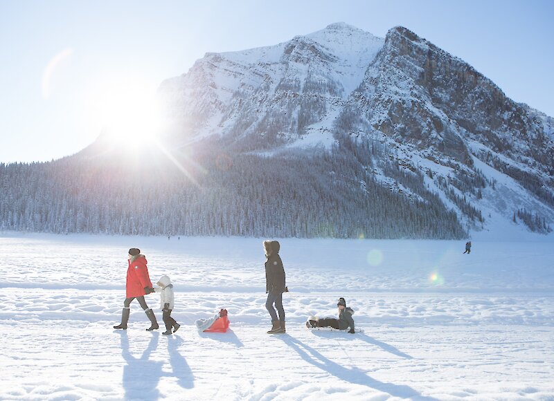 A family walking along the lake shore of Lake Louise and pulling the children on sleds